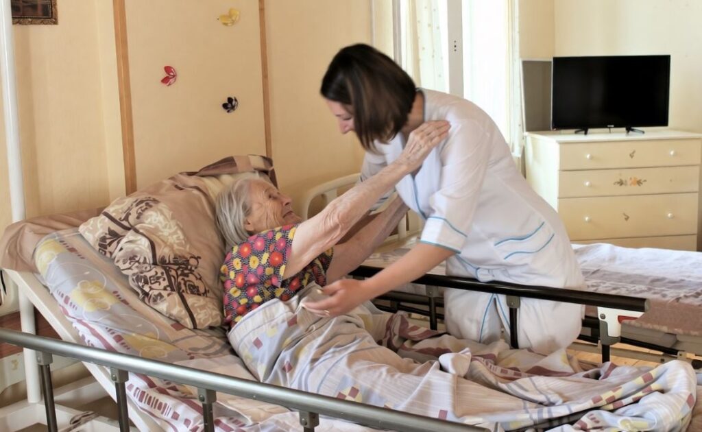 Медсестра ухаживает за лежачей пожилой женщиной в медицинской кровати